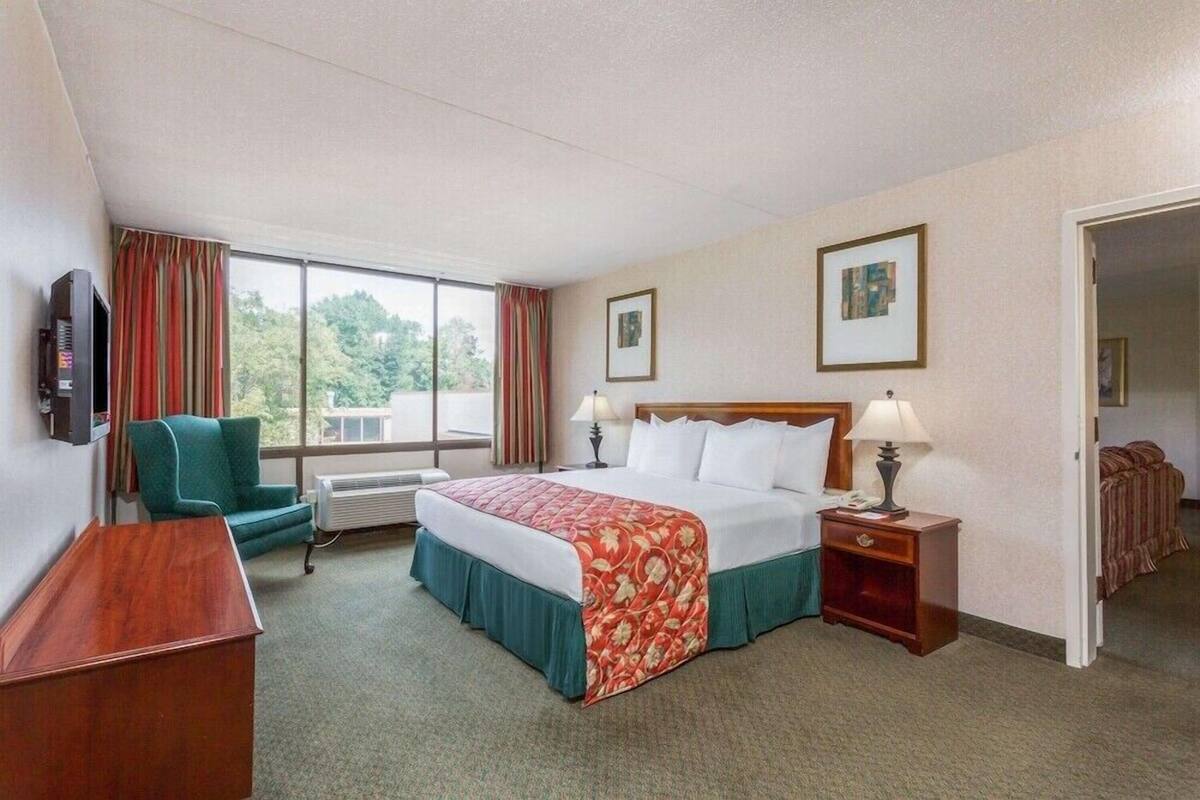 A hotel room with a bed, a desk, a chair, a TV, and a window with curtains.