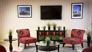 A living room with two red floral armchairs, a glass coffee table, a flat-screen TV, and a bookshelf with potted plants.