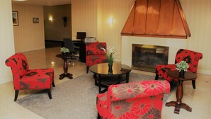 A lobby with a fireplace, red floral armchairs, a glass coffee table, and a desk with a computer.