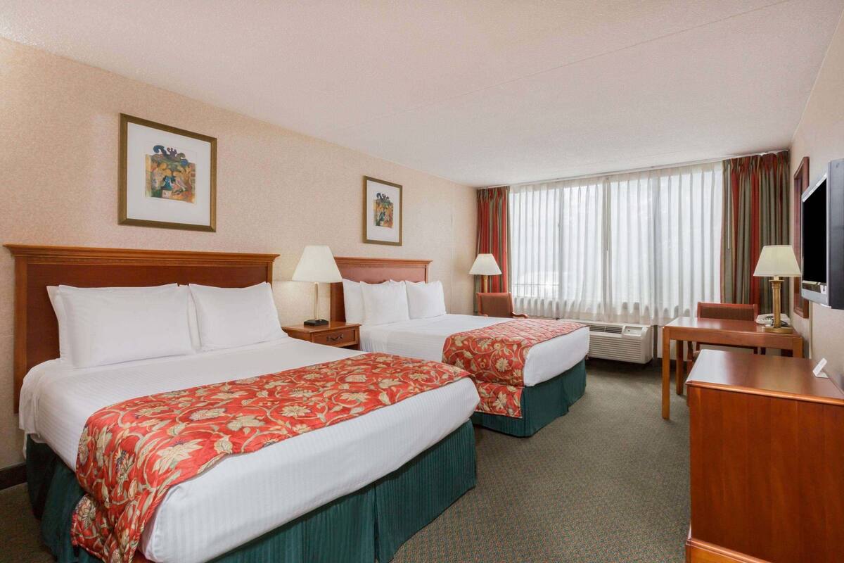 A hotel room with two beds, a desk, a chair, a TV, and a window with curtains.