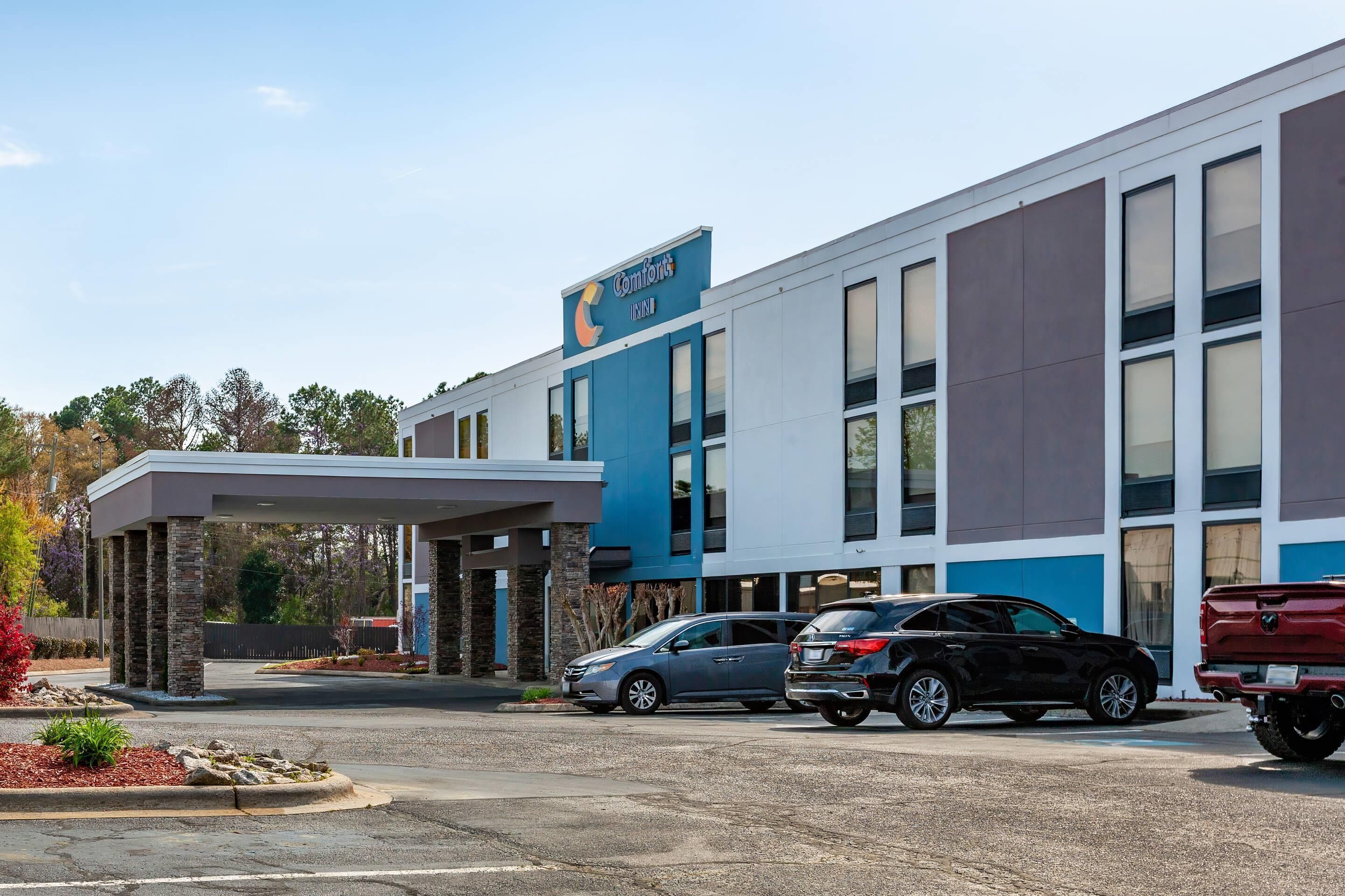 Ein modernes Gebäude mit einer blau-weißen Fassade, einem überdachten Eingang und einem Parkplatz mit mehreren Autos.