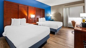 A hotel room with two beds, a desk, a chair, and a window with curtains.
