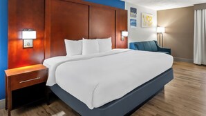 A hotel room with a large bed, wooden headboard, bedside lamps, a nightstand, and a blue armchair.