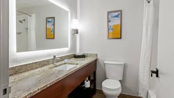 Un baño con lavamanos de encimera de granito, inodoro blanco, un cuadro en la pared y cortina de ducha.