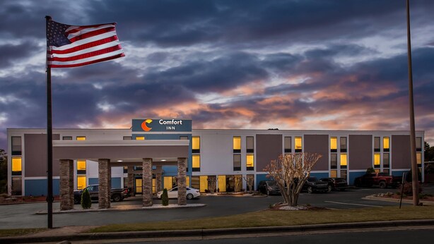 A Comfort Inn hotel with a flag, parking, and a sunset sky.