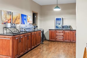 A kitchen with wooden cabinets, a countertop with appliances, and wall art. - Comfort Inn Laurinburg (Laurinburg)