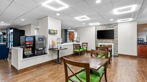 A restaurant with wooden tables and green cushioned chairs, a coffee machine, and a TV mounted on the wall.