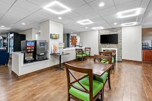 A restaurant with wooden tables and green cushioned chairs, a coffee machine, and a TV mounted on the wall. - Comfort Inn Laurinburg (Laurinburg)