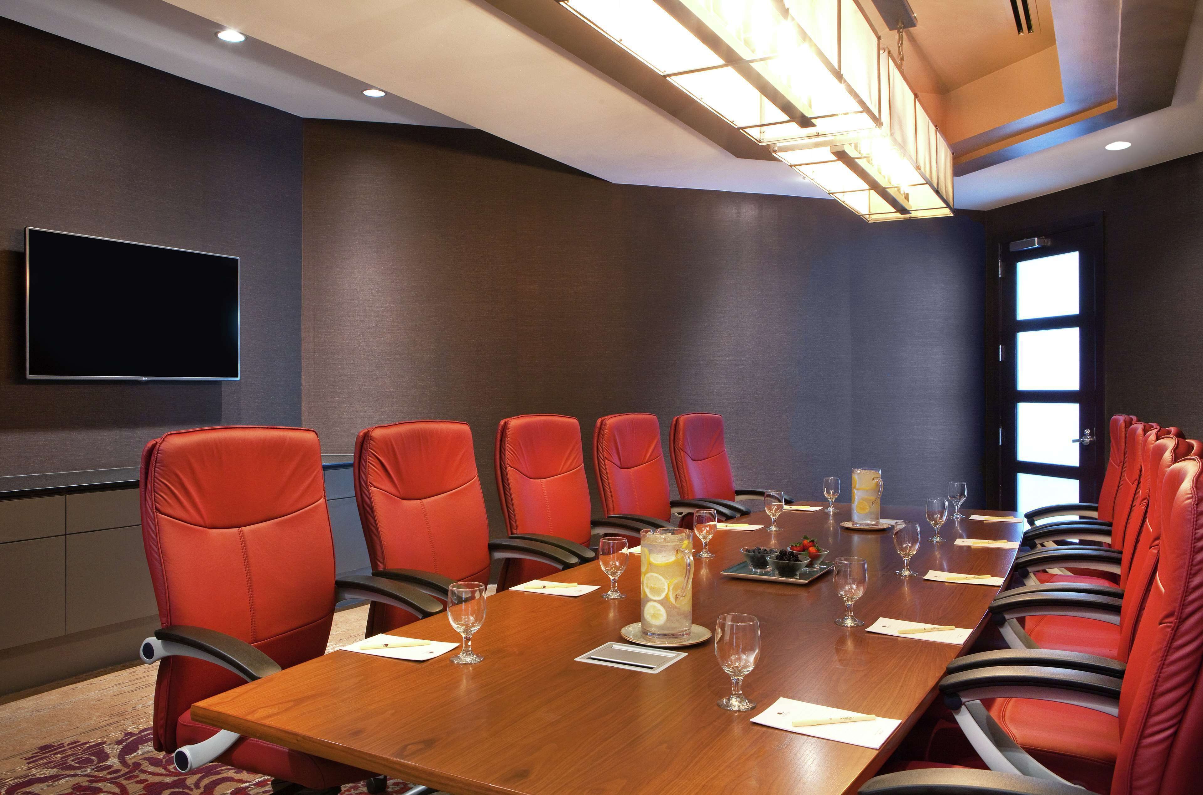 A conference room with a long table, red chairs, and a flat-screen TV on the wall.
