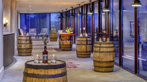 Uma área de bar moderna com barris de madeira como mesas, banquetas e uma grande janela com vista.