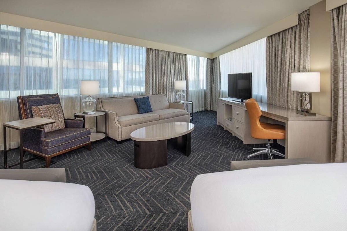 A hotel room with a bed, a sofa, a coffee table, a TV, and a desk with a chair.