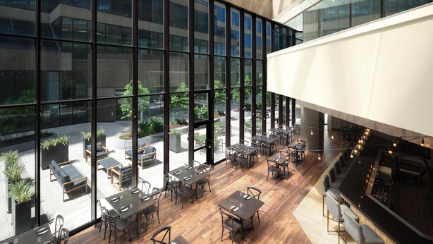 Um restaurante moderno com grandes janelas, piso de madeira e área externa para refeições.