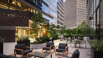 An outdoor seating area with modern furniture, surrounded by greenery and tall buildings.