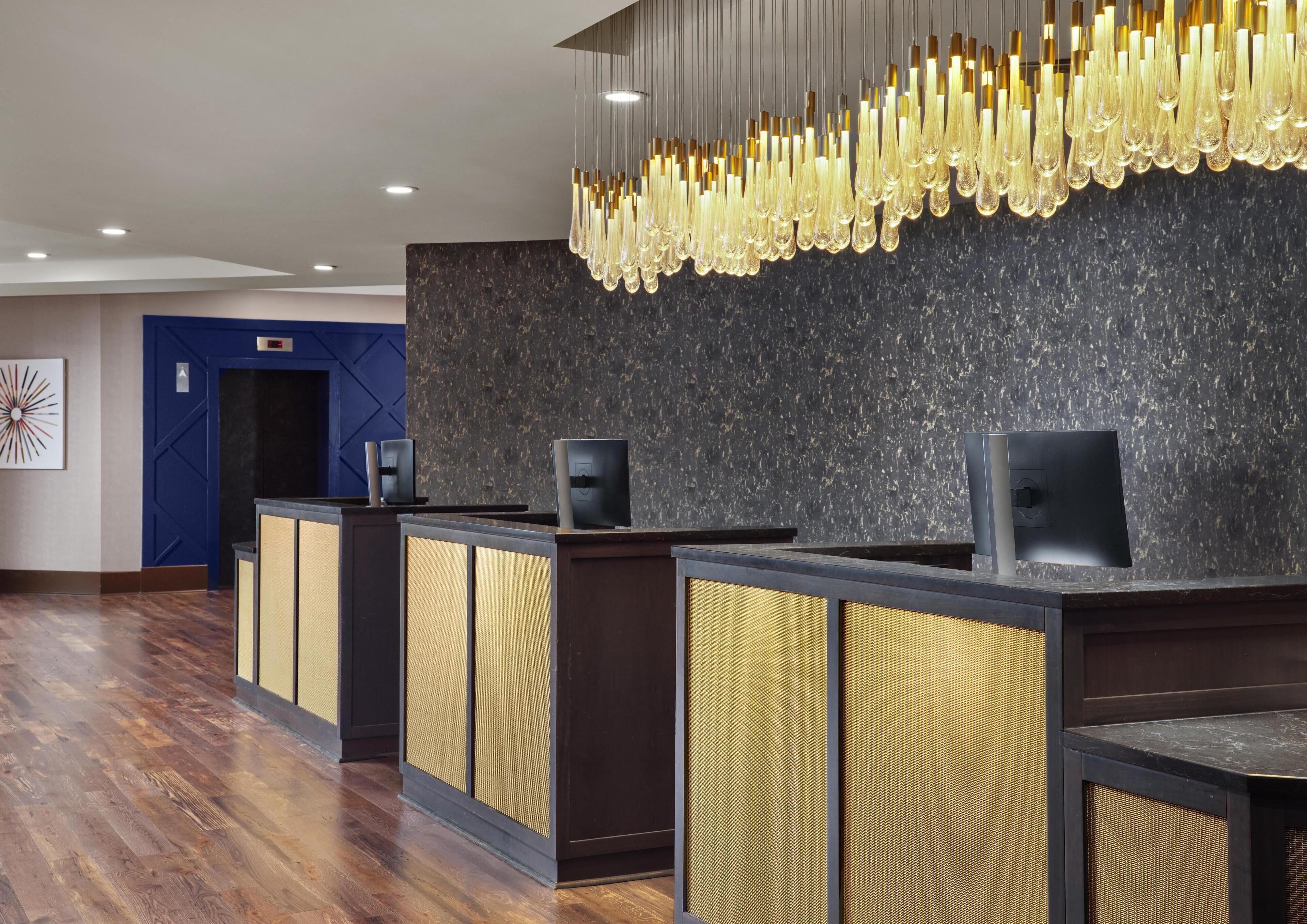 Ein Empfangsbereich im modernen Design mit dunkler Marmorwand, einem außergewöhnlichen Chandelier und einem Holzbüro mit Webpanel-Design.