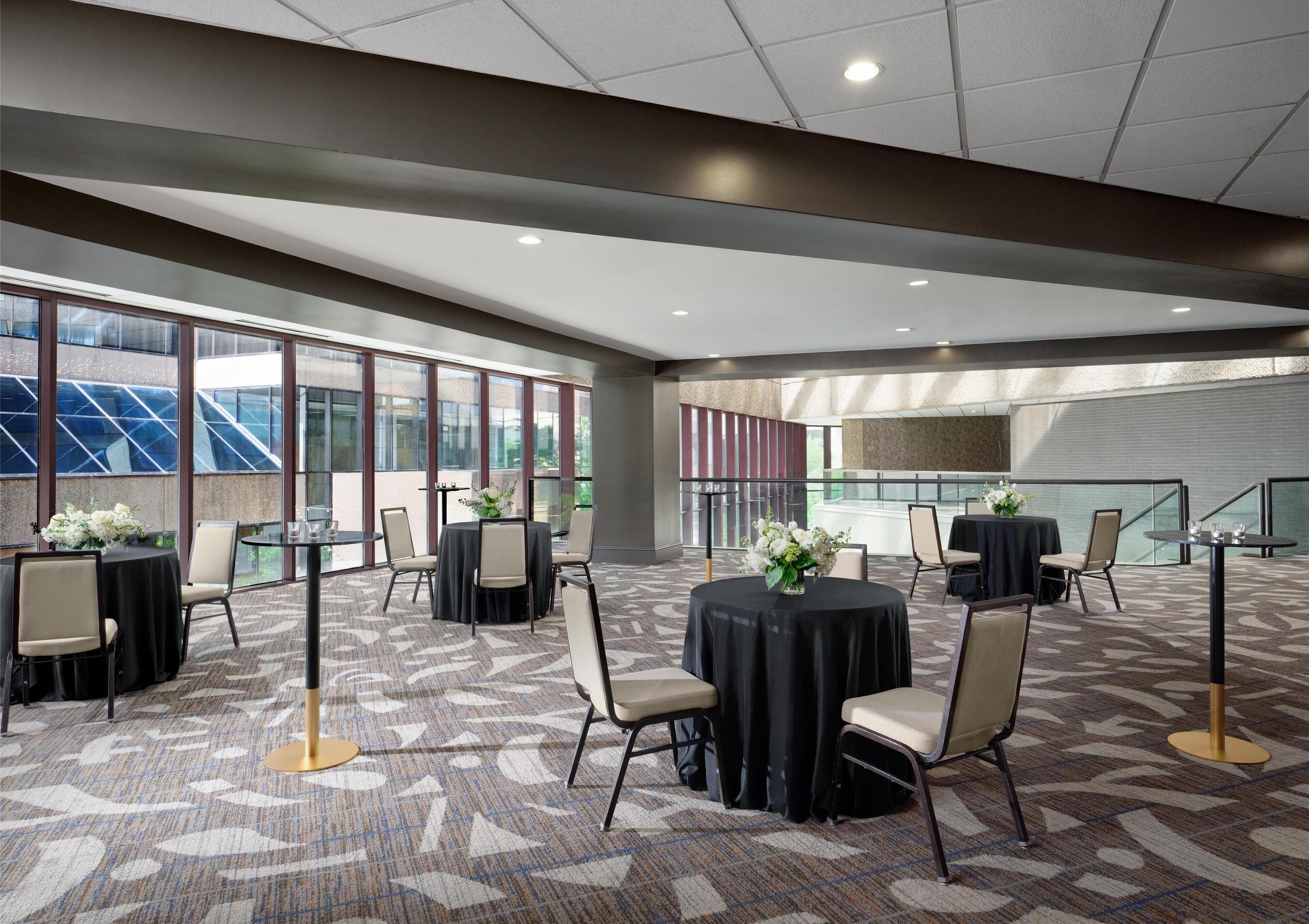 A spacious conference room with large windows, multiple tables with chairs, and a patterned carpet.