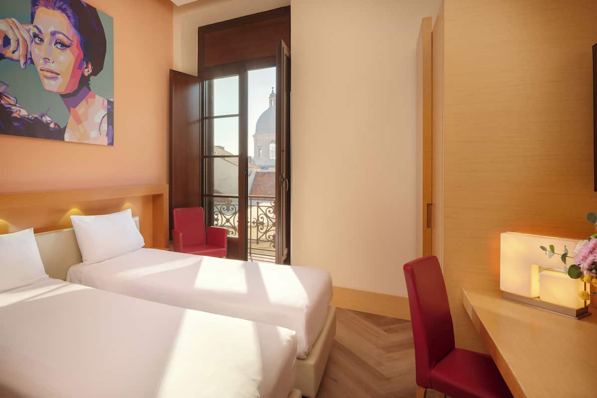 Een hotelkamer met twee bedden, een rode stoel, een bureau met een lamp en een schilderij aan de muur.