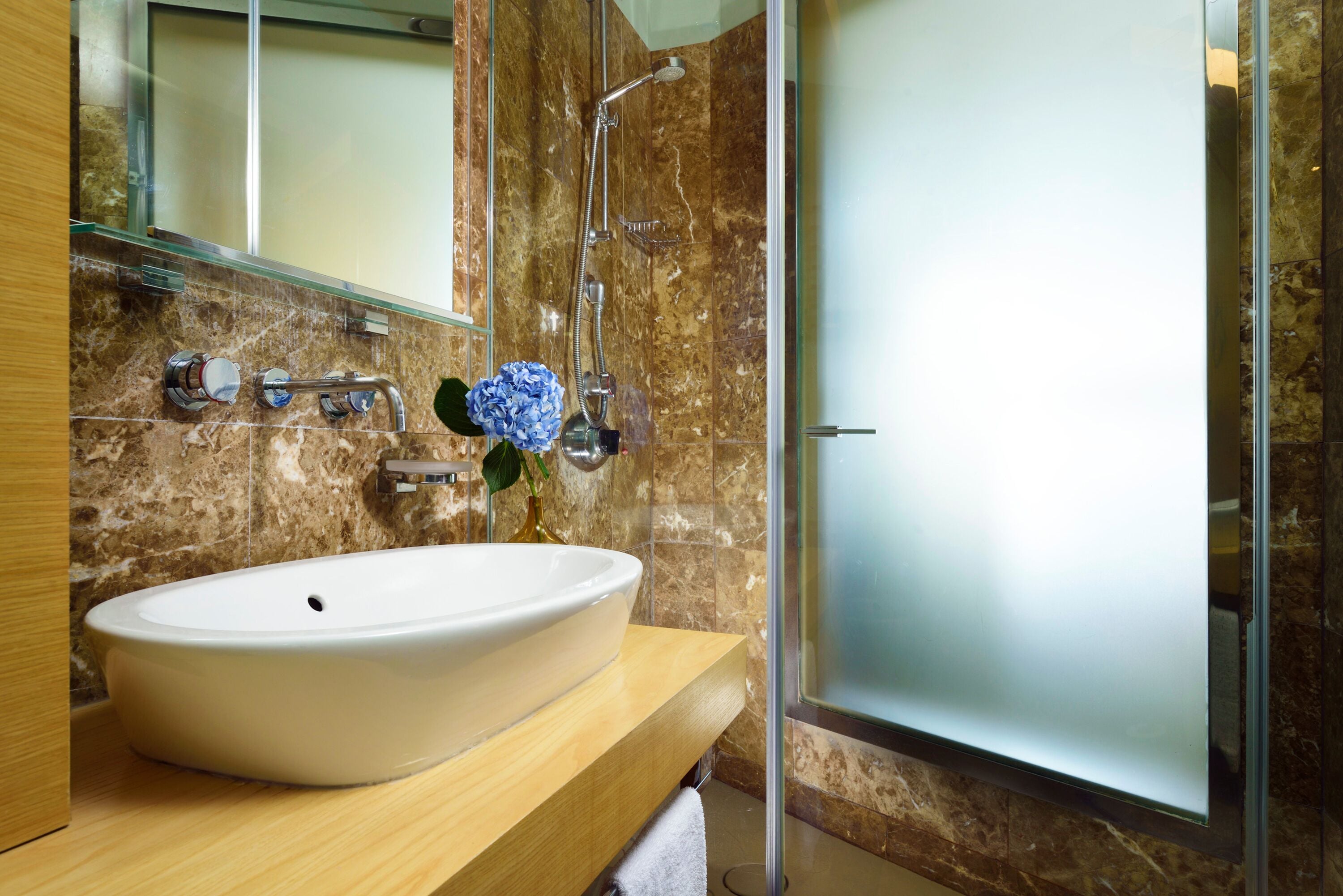 Un bagno con un lavandino bianco, cabina doccia in vetro e parete rivestita in marmo.