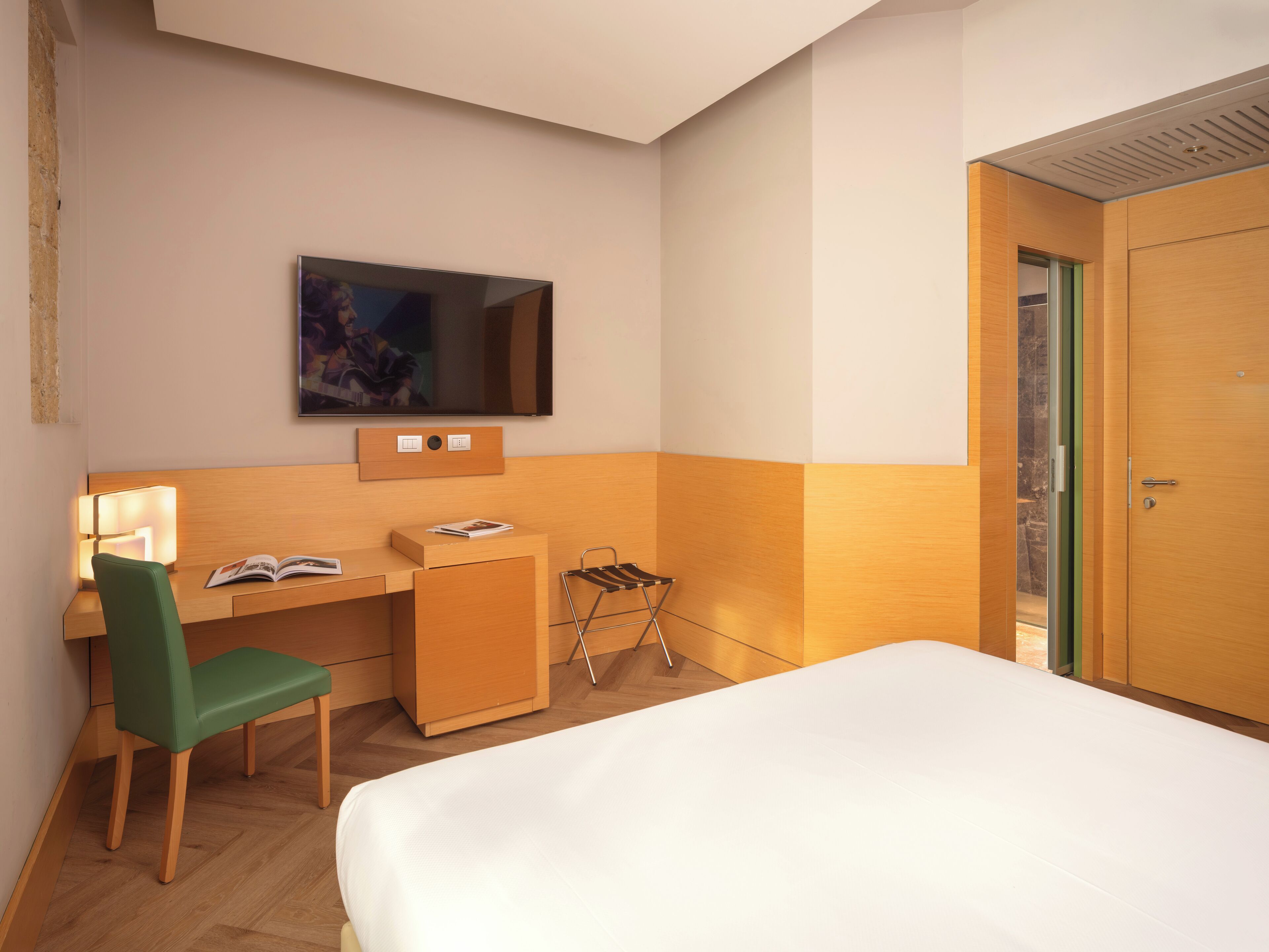 Een hotelkamer met een bed, een bureau met stoel, een aan de muur bevestigde televisie en een kledingkast.