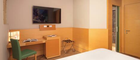 Ein Hotelzimmer mit Bett, Schreibtisch mit Stuhl, Wandfernseher und Kleiderschrank.