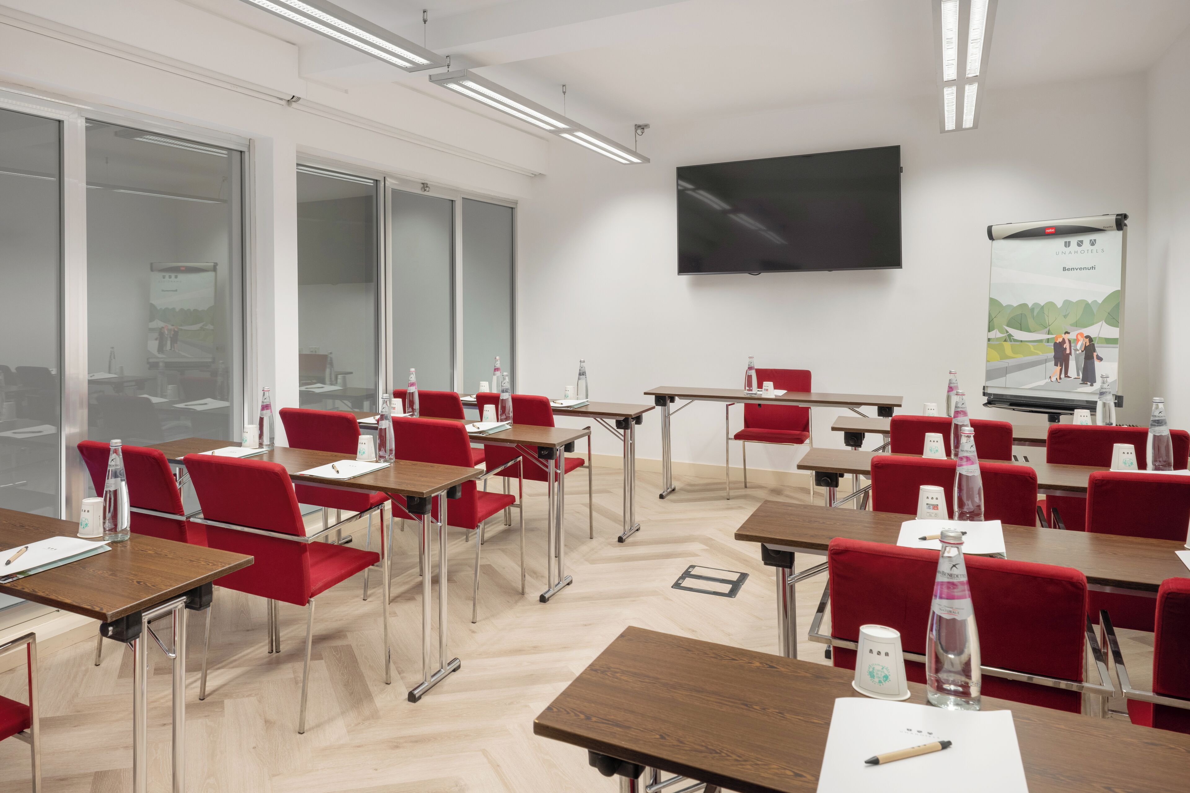 A conference room with red chairs, wooden tables, a flat-screen TV, and a presentation screen.