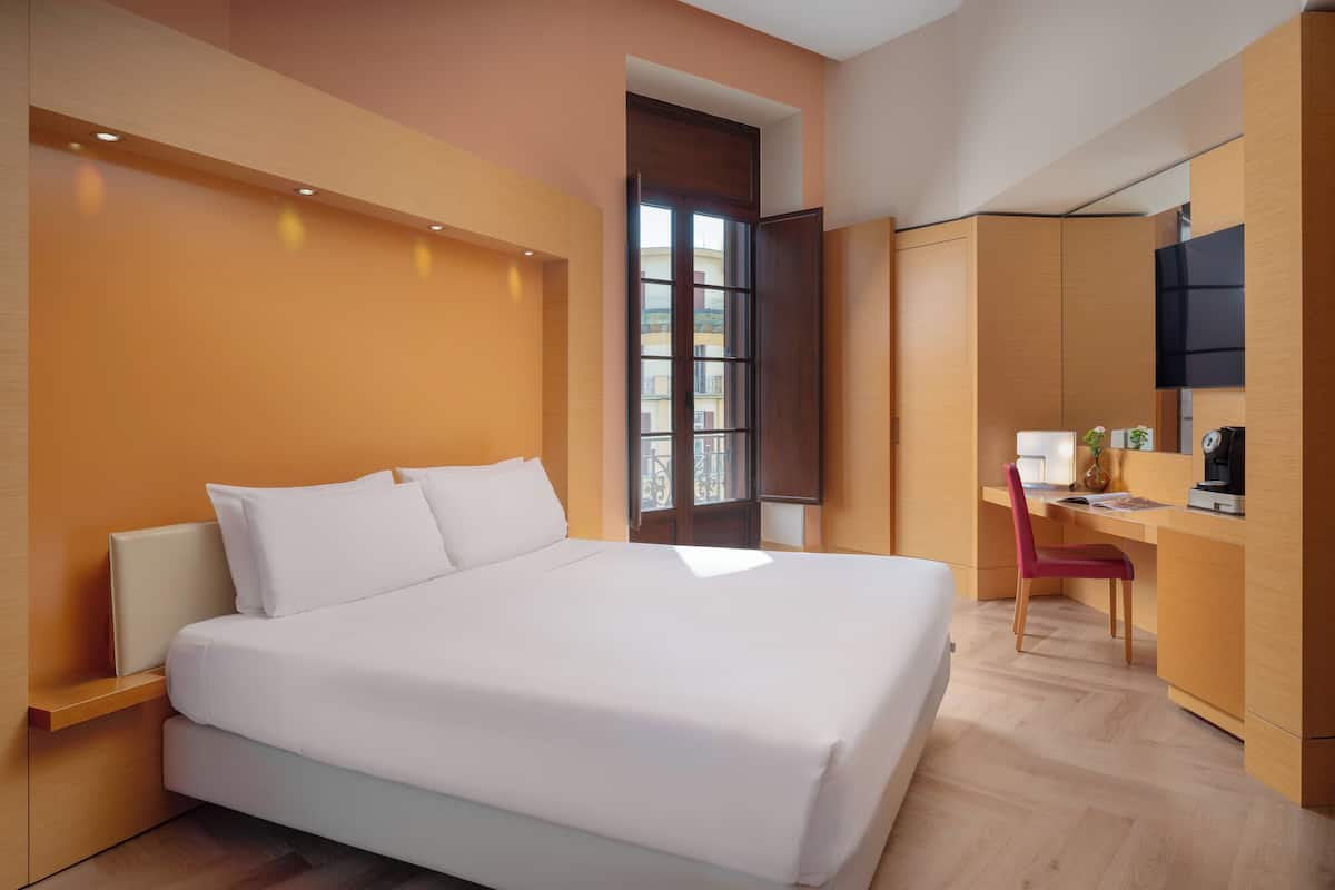 Een moderne hotelkamer met een groot bed, een bureau met stoel en een aan de muur bevestigde televisie.