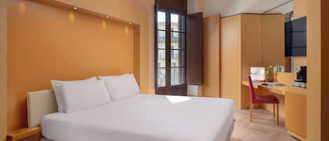 A modern hotel room with a large bed, a desk with a chair, and a TV mounted on the wall.