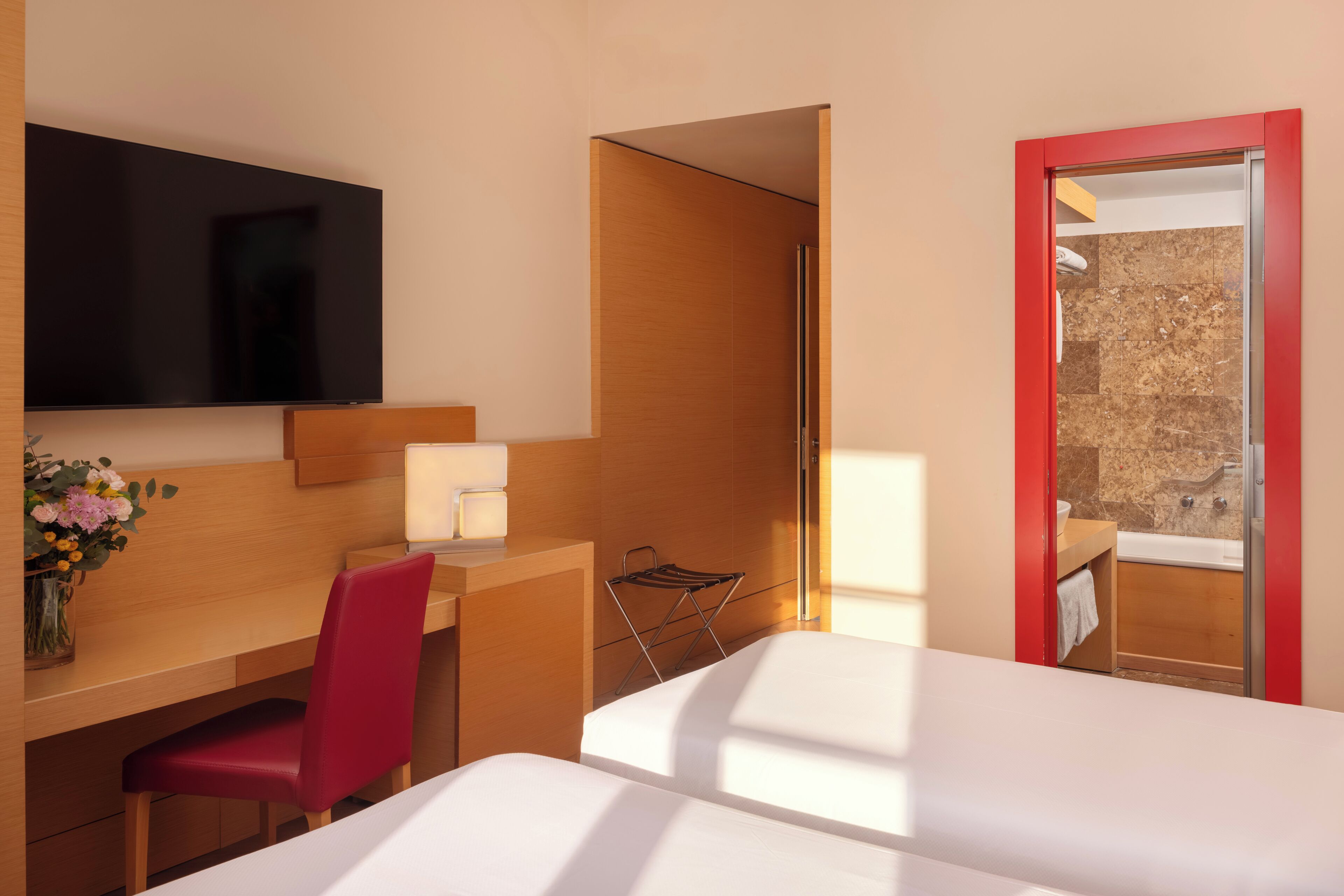 Habitación de hotel con cama, escritorio con silla, televisor y zona de ducha.