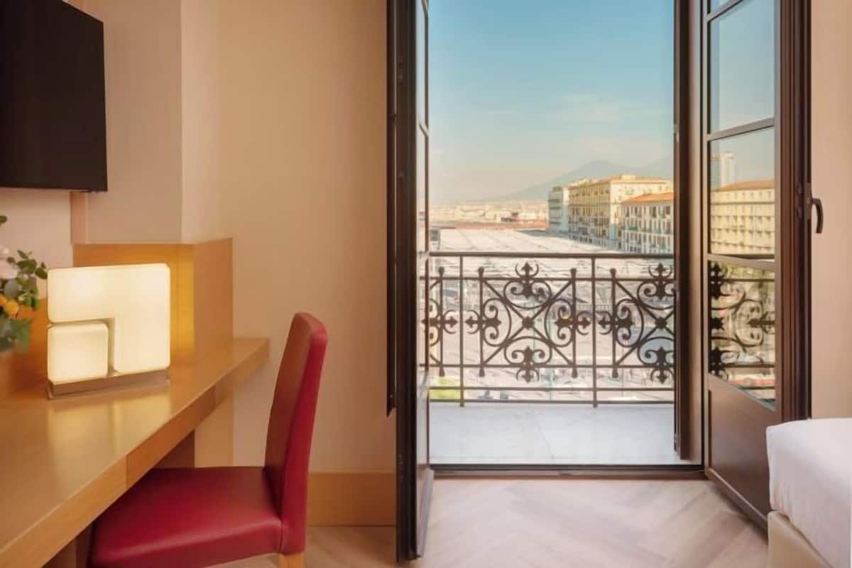 Een hotelkamer met balkon, bureau met stoel, televisie en bed.