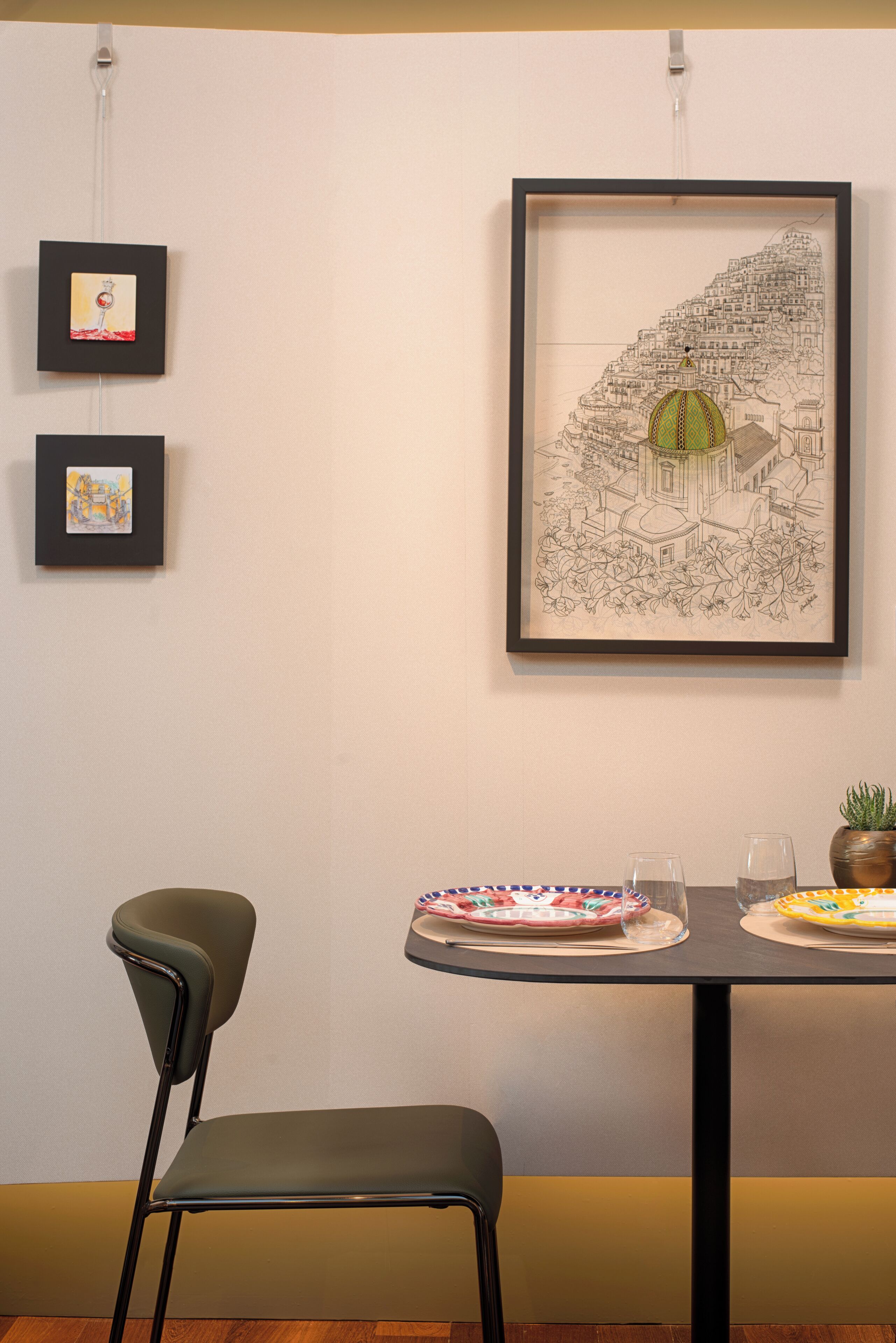 A dining table with two chairs, a framed artwork above, and a potted plant on the table.