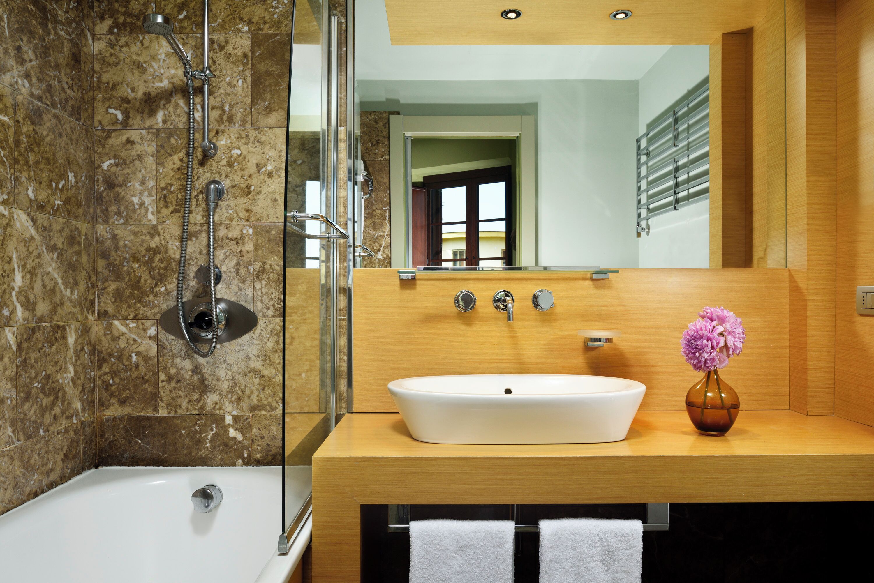 A modern bathroom with a bathtub, a large mirror, and a wooden vanity with a sink.