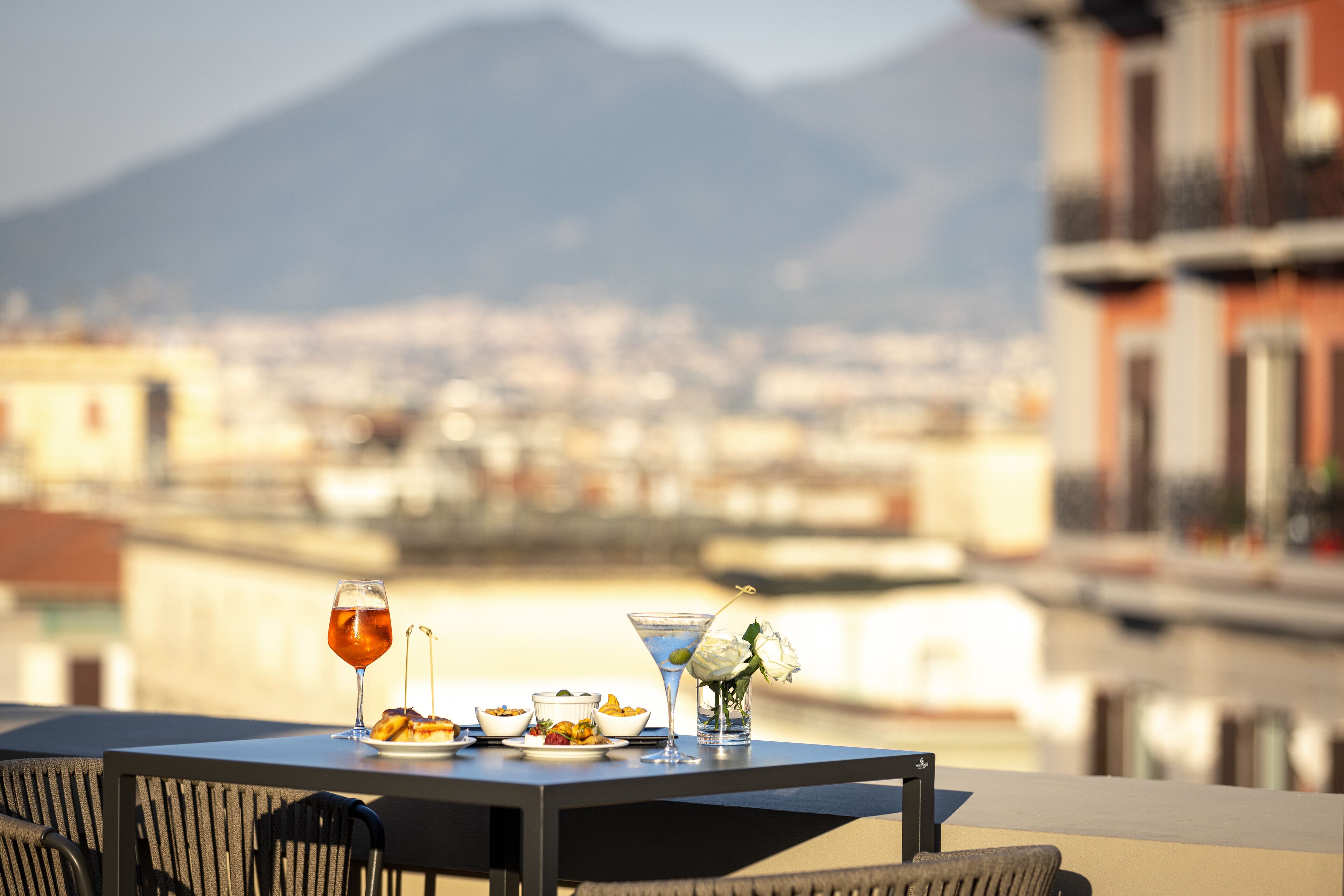 Une table dressée avec un repas et des boissons, donnant sur un paysage urbain avec des montagnes en arrière-plan.