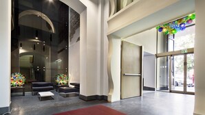 A modern lobby with a curved glass wall, seating area, and a glass door entrance. - UNA Hotels Napoli (Naples)
