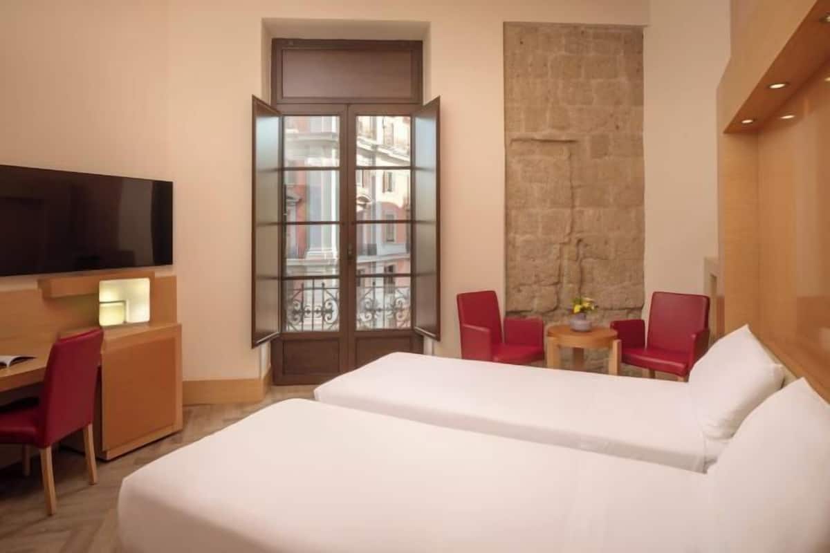 Een hotelkamer met een bed, een bureau, een televisie, een rode stoel en uitzicht.