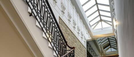 A marble staircase with ornate black iron railings leading to a glass-paneled upper level.