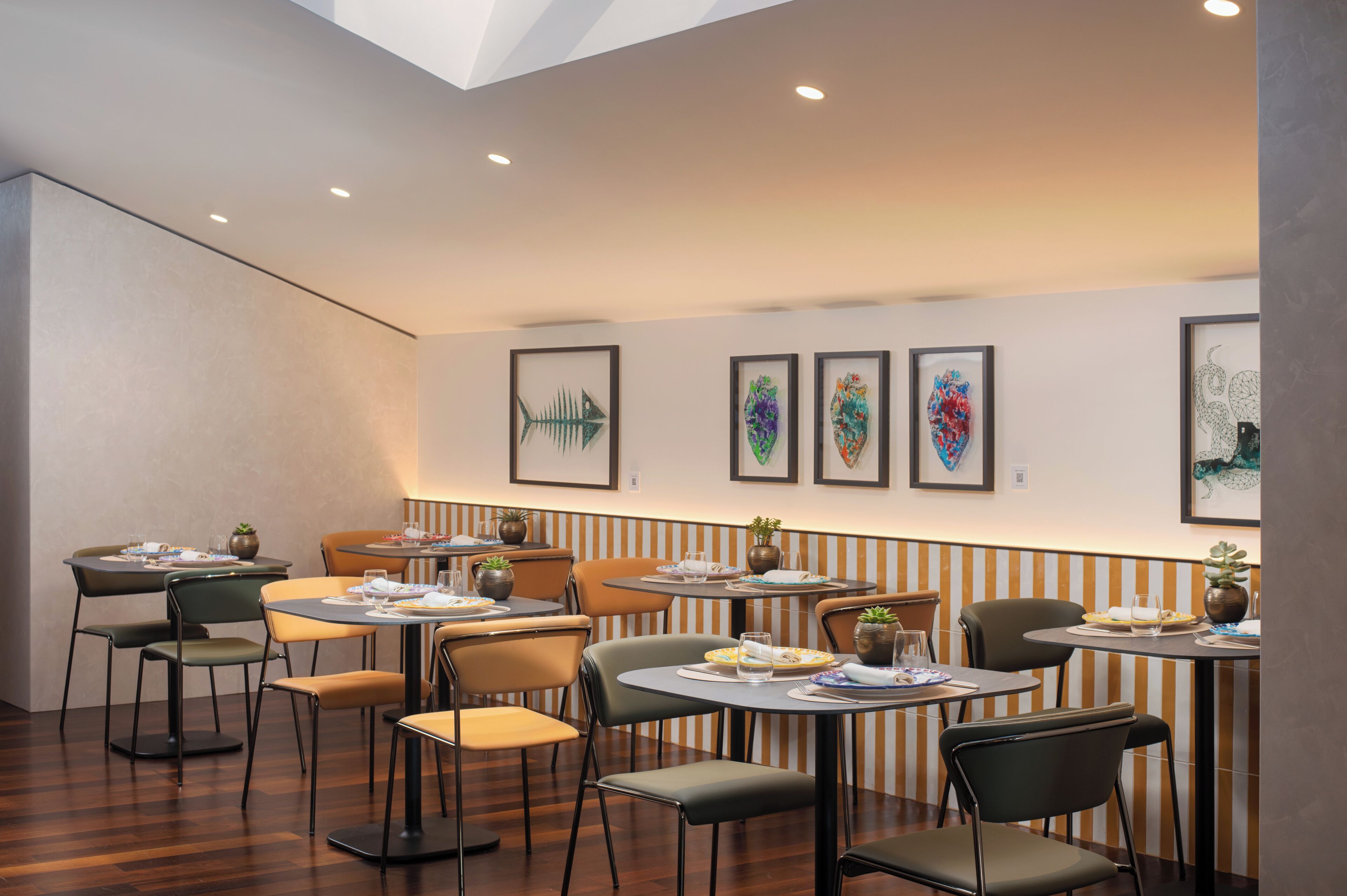 A restaurant with tables and chairs, framed artwork on the walls, and ceiling lights.