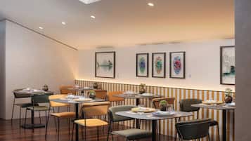 Ein Restaurant mit Tischen, Stühlen, gerahmten Kunstwerken an den Wänden und Deckenleuchten.