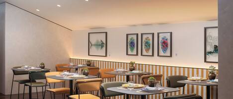 A restaurant with tables and chairs, framed artwork on the walls, and ceiling lights.