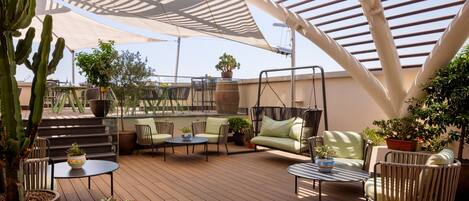 An outdoor patio with wooden flooring, cushioned seating, and potted plants.