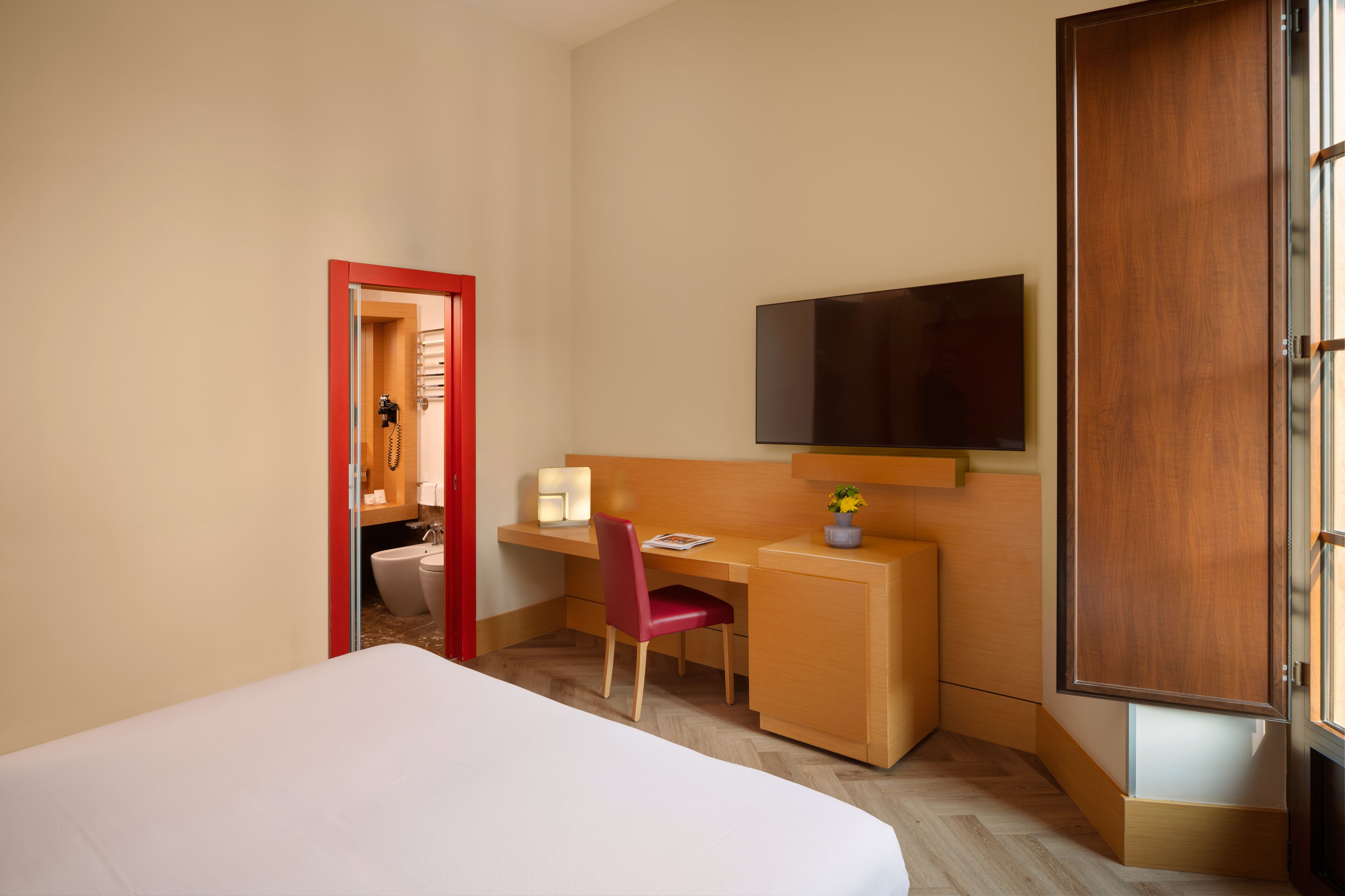 Une chambre d’hôtel avec un lit, un bureau, une chaise, une télévision et une porte.