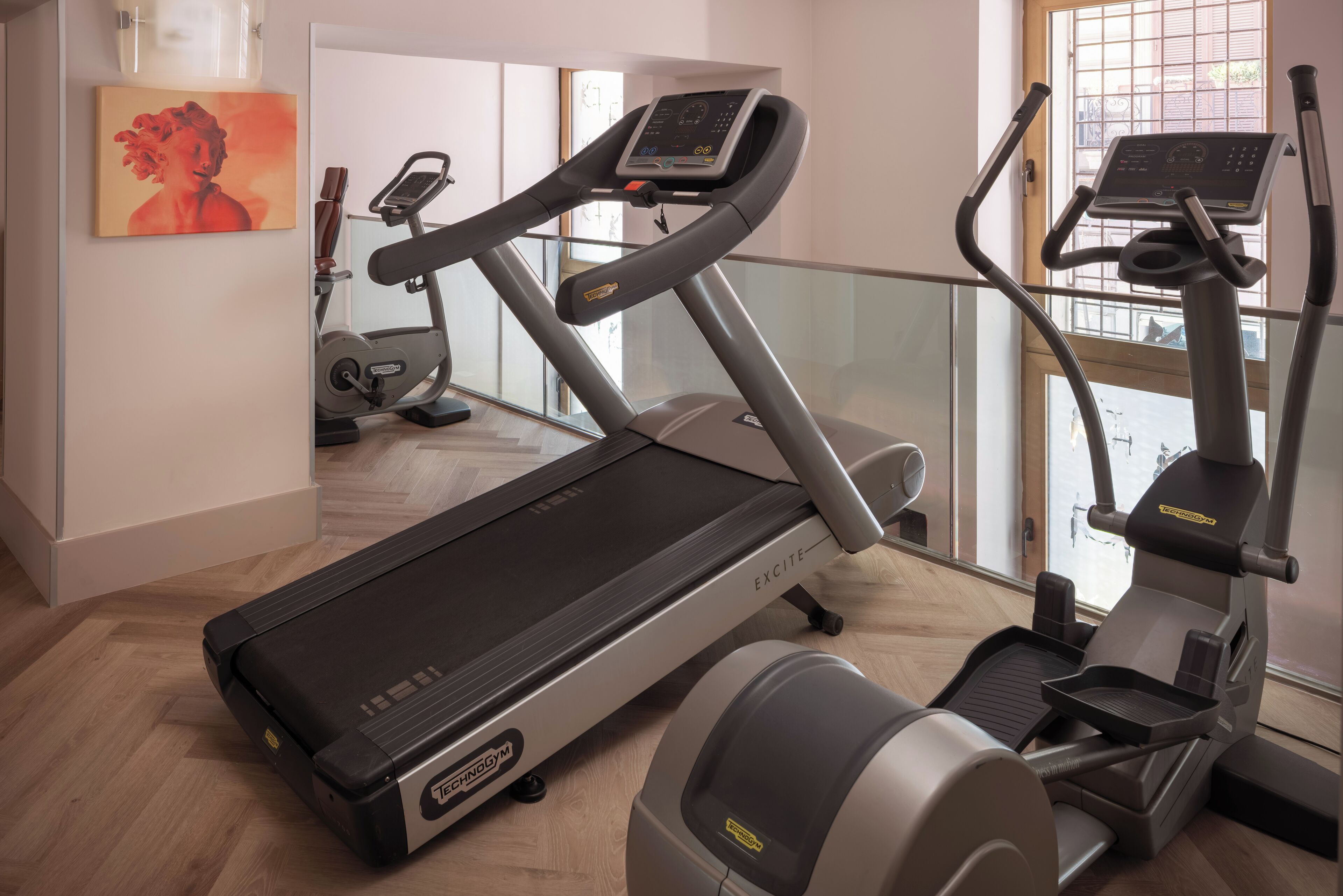 Et hjemmegymnasium med løbebånd, crosstrainer og motionscykel, med trægulv og store vinduer.