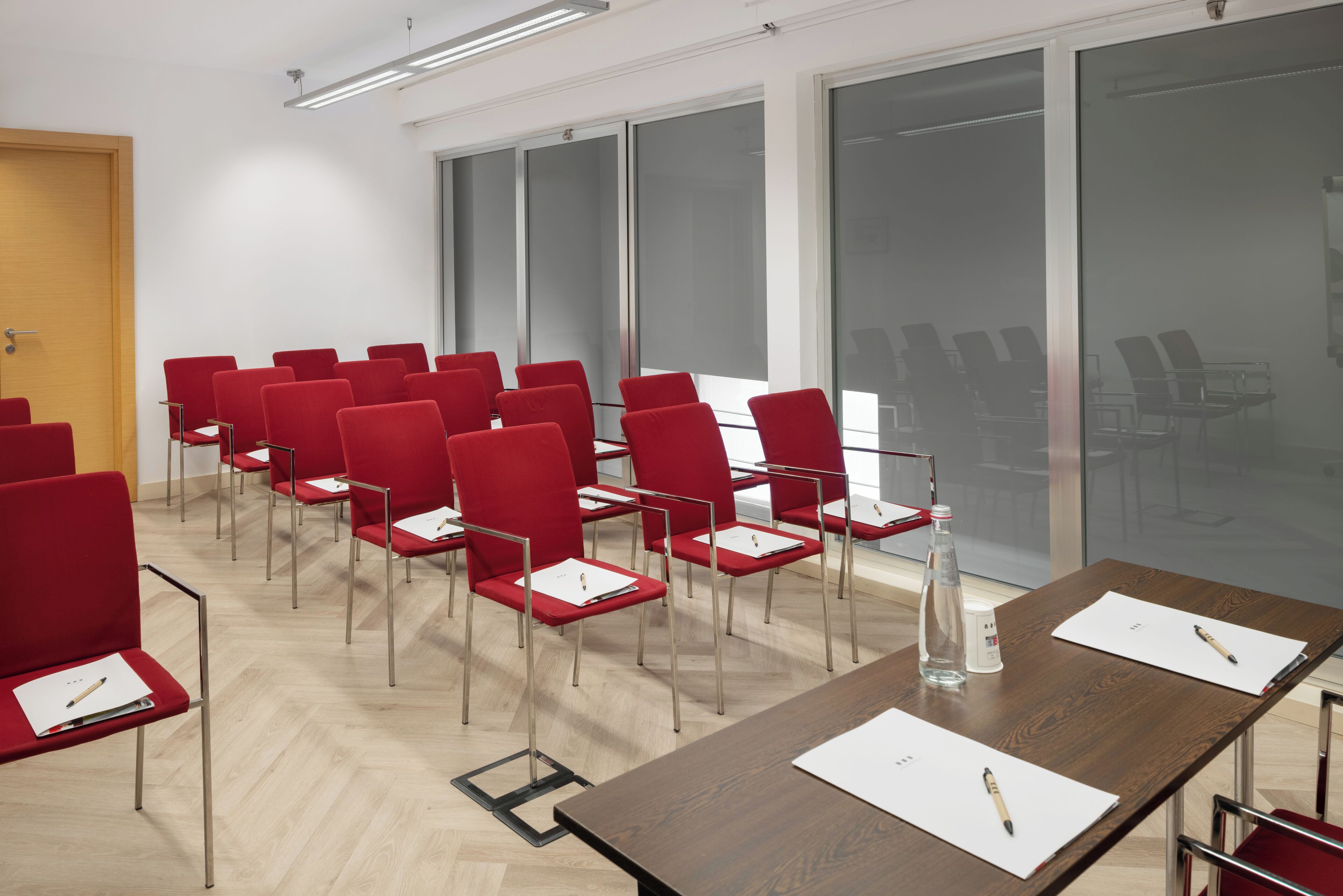 A conference room with red chairs, a wooden table, and a large window.