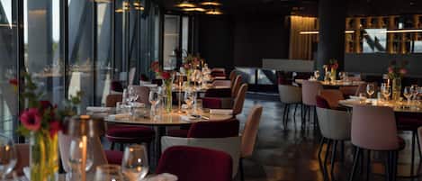 A restaurant with tables set for dining, featuring modern decor and a view through large windows.