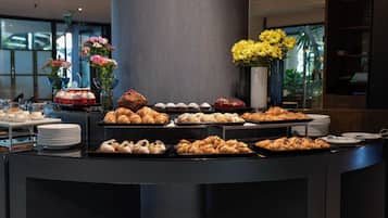 A buffet counter with various pastries and desserts, including croissants and cakes, arranged on trays.