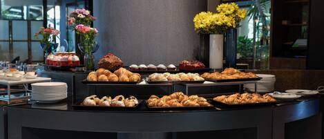 A buffet counter with various pastries and desserts, including croissants and cakes, arranged on trays.