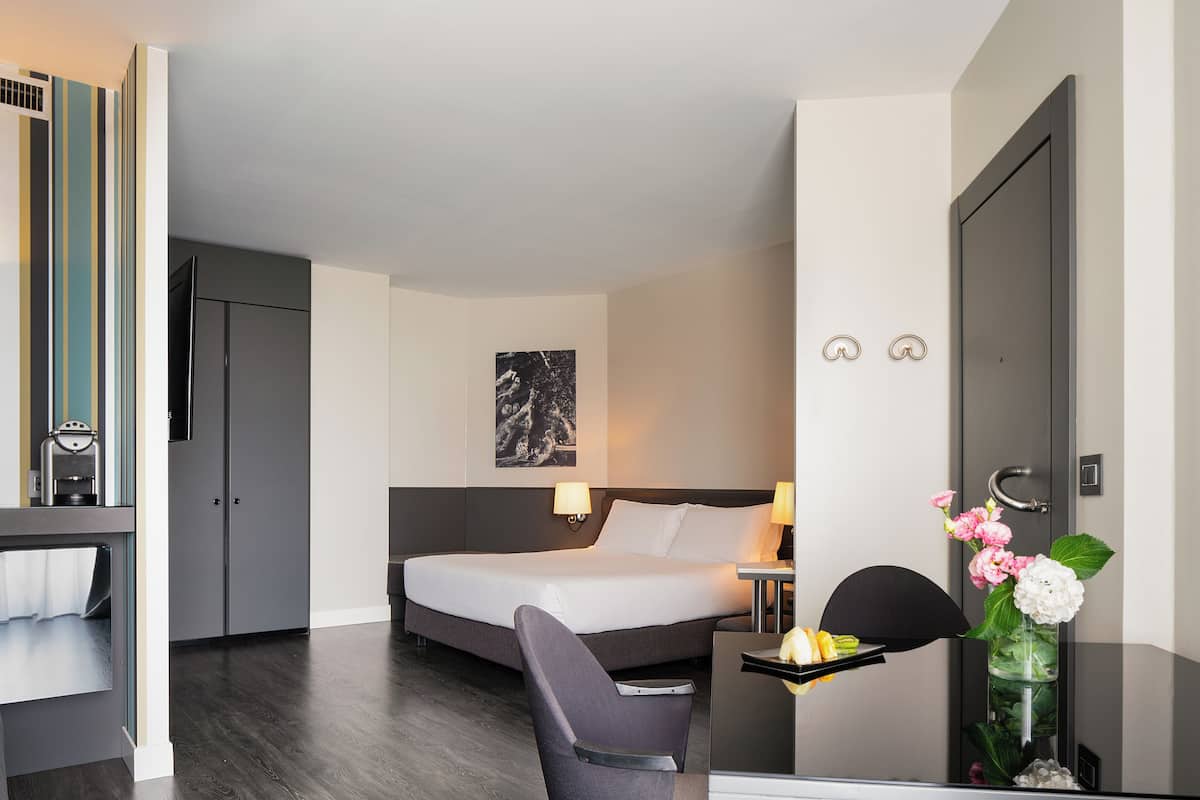 Una habitación de hotel con cama, mesita de noche, silla, escritorio y una pequeña mesa con flores.