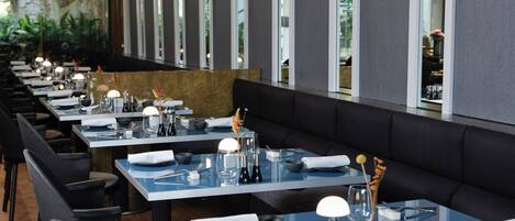 A modern restaurant with long tables, black chairs, and pendant lighting.