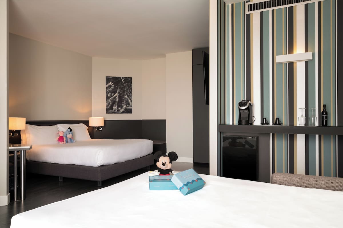 Habitación de hotel con cama, un peluche de Mickey Mouse y una barra de desayuno, todo con un diseño de papel tapiz a rayas.