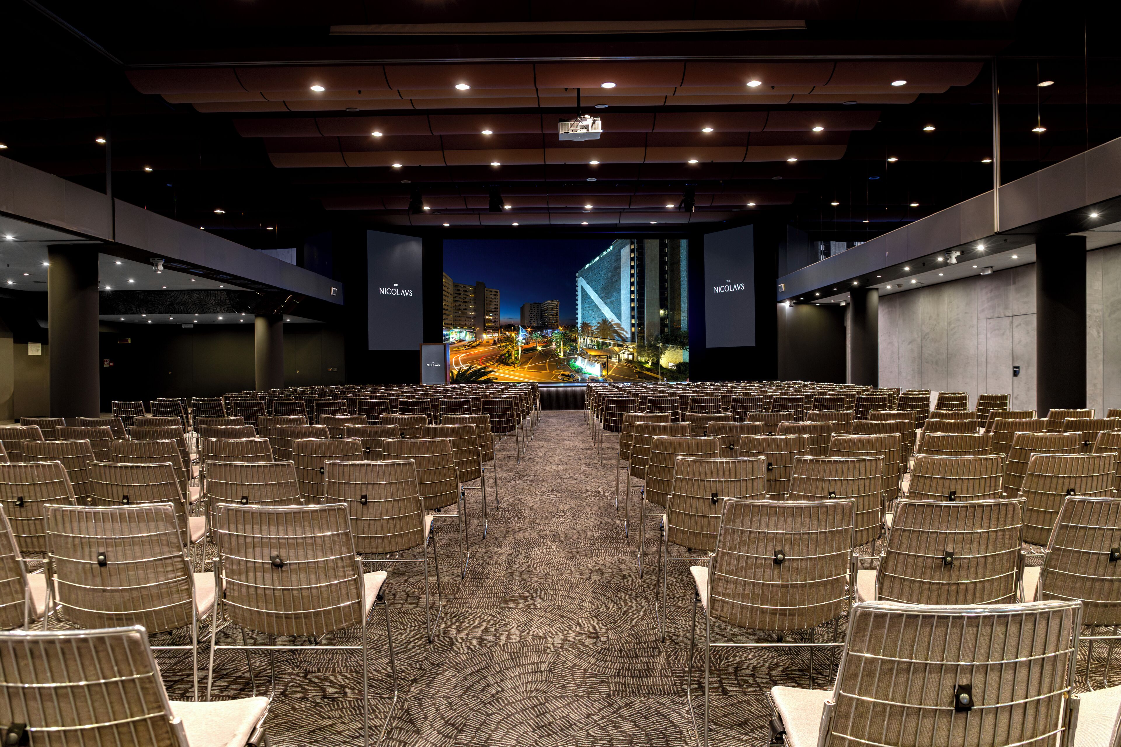 A conference room with rows of chairs facing a large screen displaying a cityscape.
