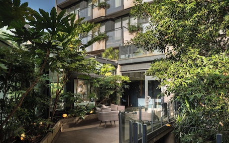 A modern building with a glass balcony, lush greenery, and outdoor seating.
