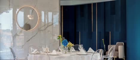 A modern dining room with a marble wall, a round mirror, and a blue accent wall.